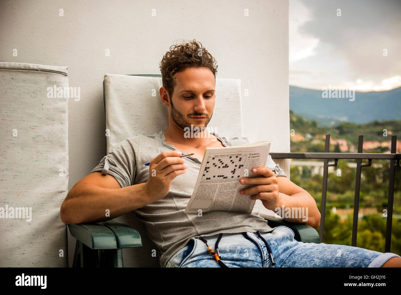 Young Man Sitting Doing A Crossword Puzzle Looking Thoughtfully At A